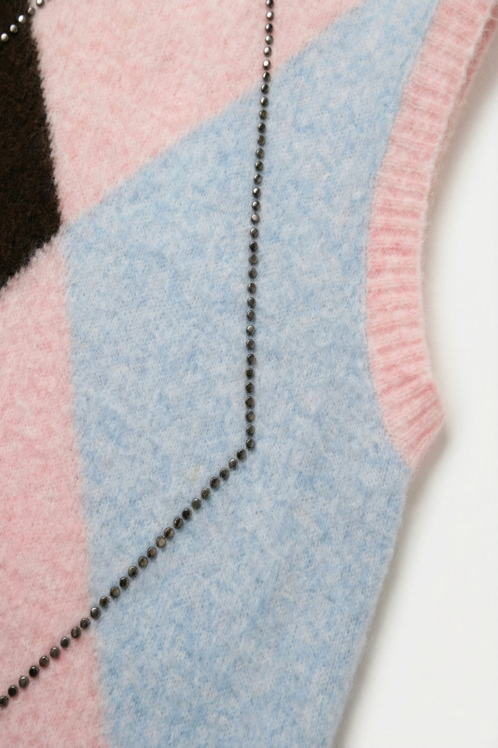 Colete de malha com estampado de losangos e detalhes de tachas metálicas em cor-de-rosa.