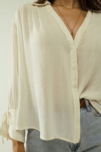 Camisa branca clara com decote em V e pormenores de riscas